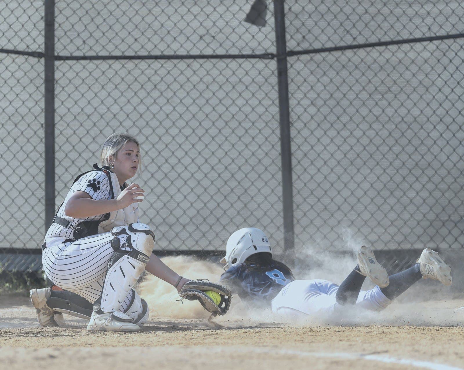 Softball runner slides into home plate in a cloud of dust